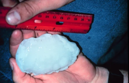 A hailstone held in two hands, measured against a ruler